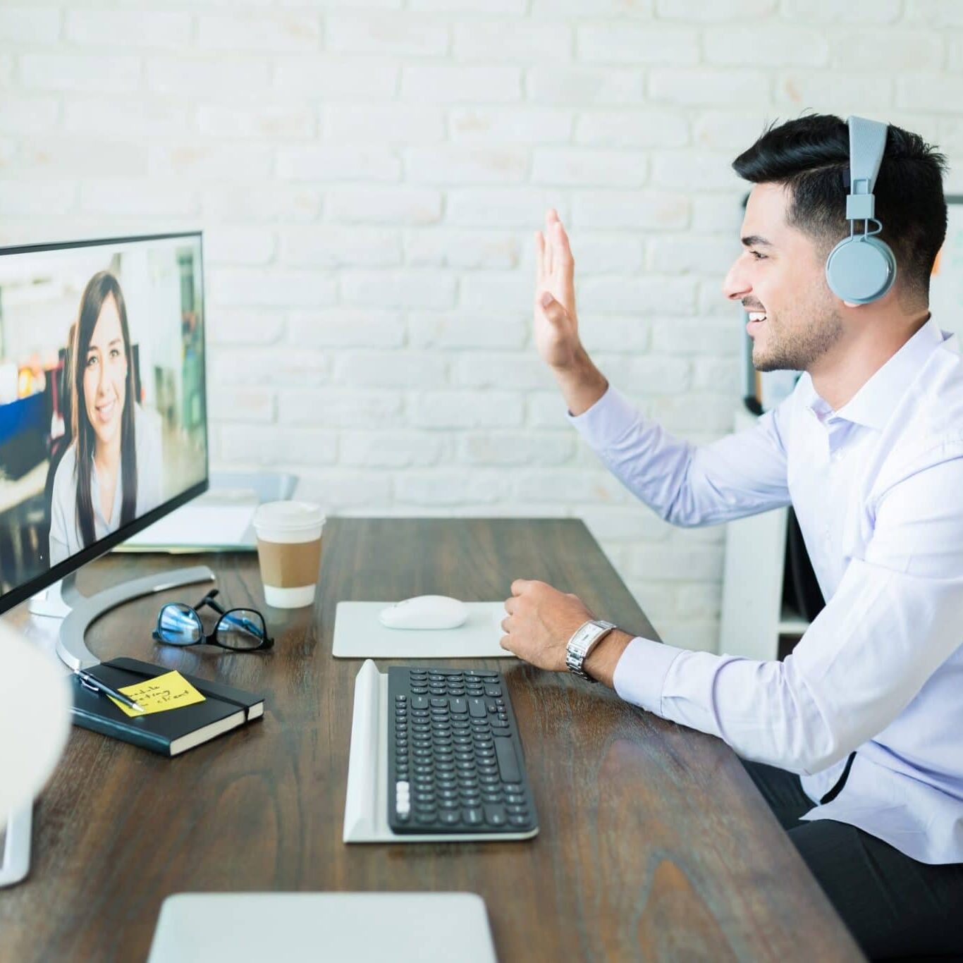 Confident young salesman waving at colleague during video call on computer at desk